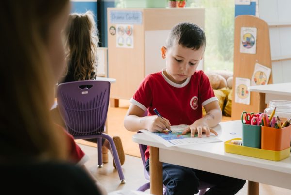 Chłopiec w czerwonej koszulce rysuje przy biurku w sali lekcyjnej Maple Bear.